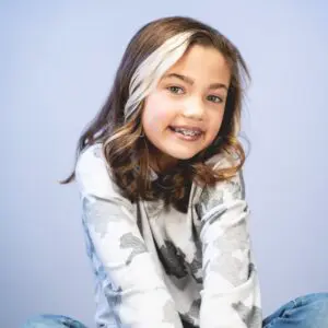 A young girl with a streak of white in her hair smiling while wearing braces